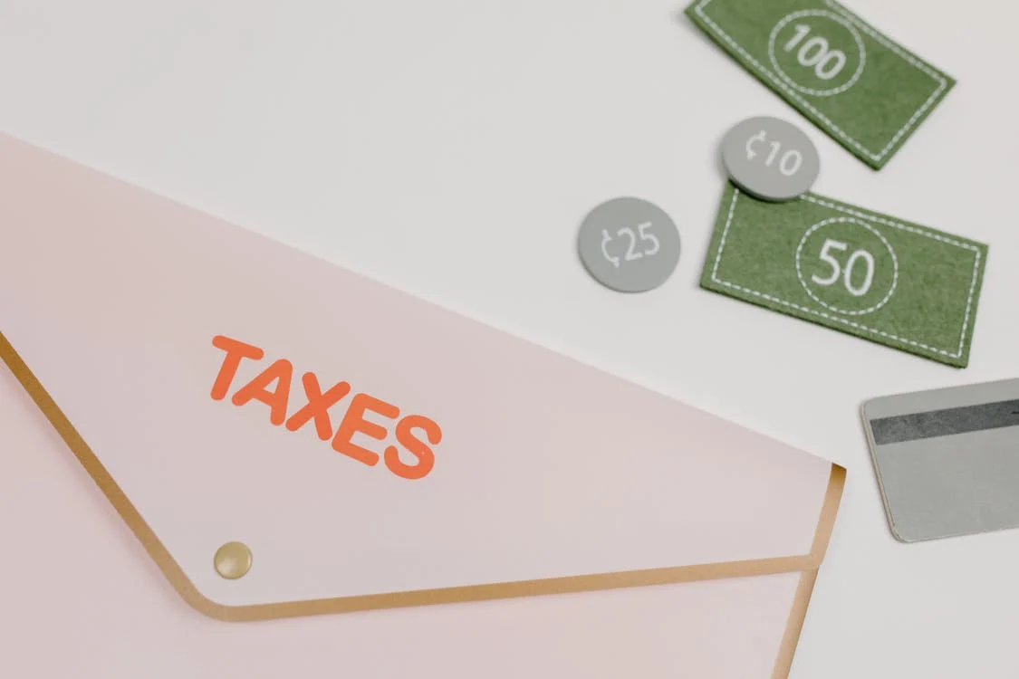 An image of an envelope with the name taxes surrounded by play money and debit card to show the importance of how to register as a freelancer on BIR